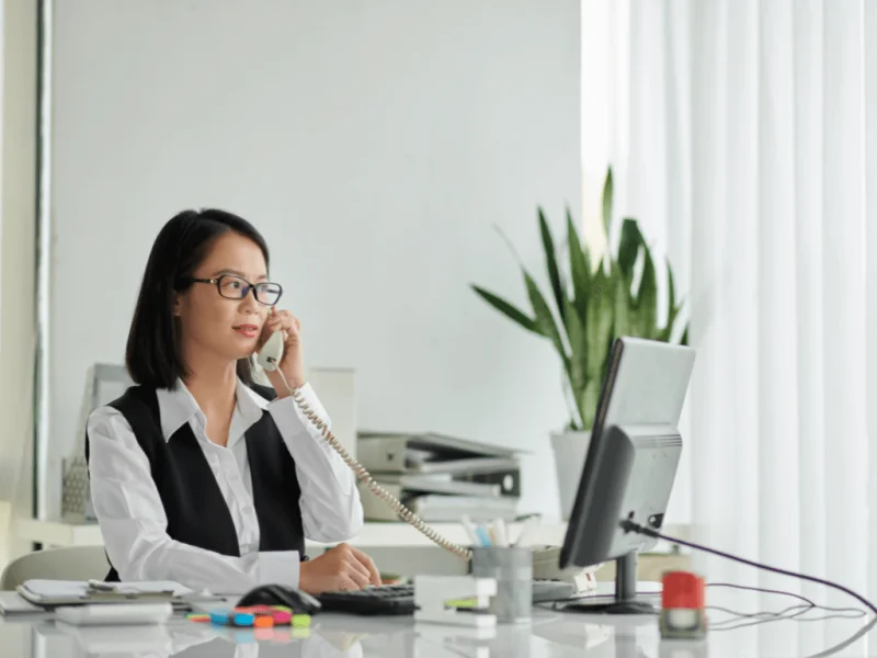 A legal assistant answers a call in her office, handling inquiries about online notarial affidavits