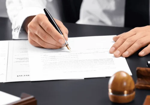 Lawyer in dark suit signing documents at desk, managing online web publication certification.