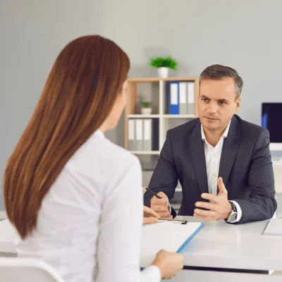 A man in a dark suit and white shirt talks with a woman in an office, reviewing the visa processing certificate online before continuing with the process.