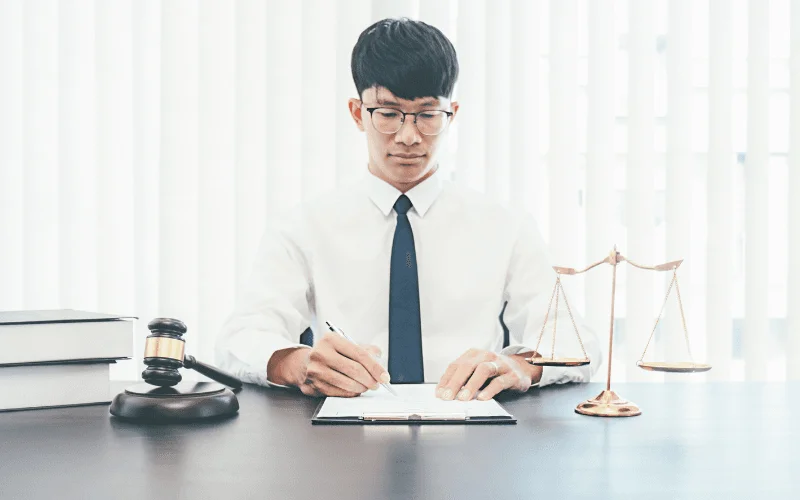 Abogado en camisa blanca y corbata firmando documentos en su escritorio, realizando el proceso de legalización de libros online.