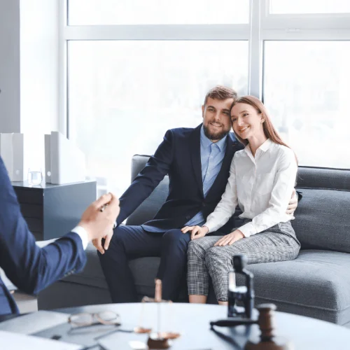 Pareja sonriente sentada en el despacho de un abogado, recibiendo asesoramiento sobre otorgamiento y revocacion de poderes online.