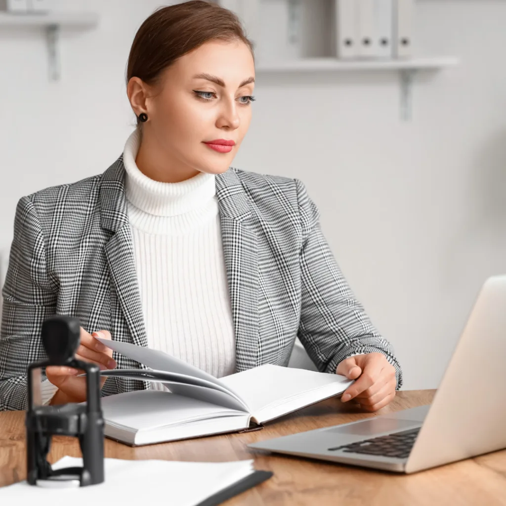 Profesional del derecho con suéter blanco y saco de cuadros, revisando documentos en su laptop mientras trabaja en el otorgamiento y revocación de poderes online.